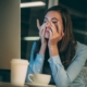 A very stressed woman with long hair at a table. She's got her head in her hands.