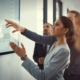 A group of people in the office looking at figures on a whiteboard. A suited women in a neat bun makes a decision.